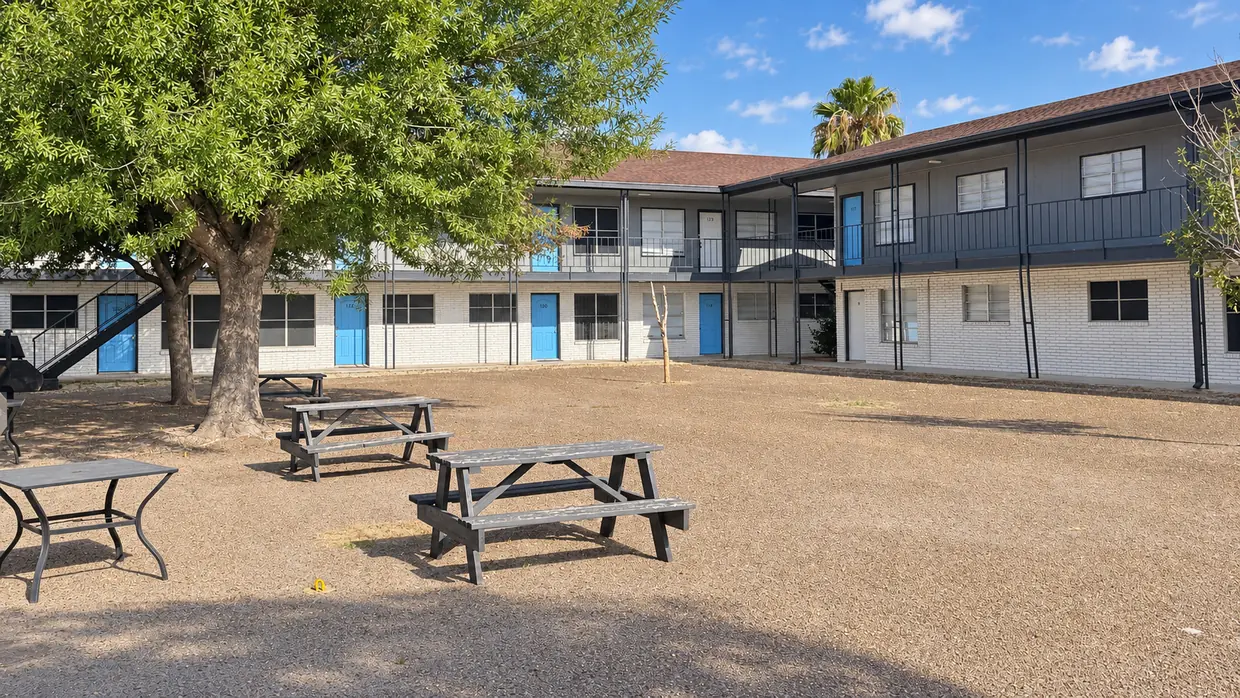 Main courtyard at The Monark Apartments, with mature shade trees, blue doors, and resident seating